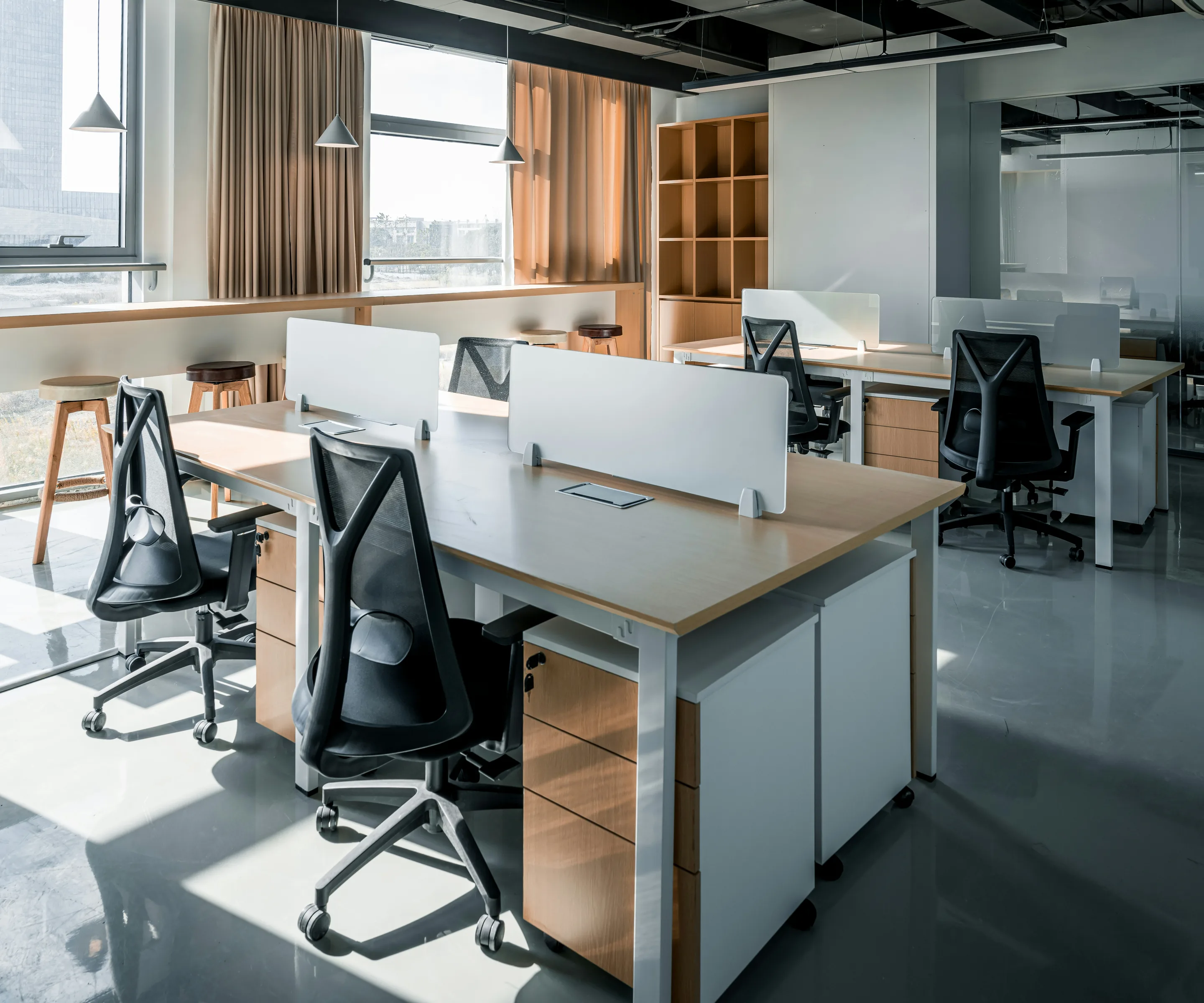Shared desks with privacy screens, mesh task chairs and wood-front storage pedestals in a sunlit open office
